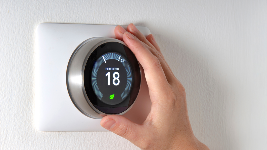 A person's hand adjusting a smart thermostat on a white wall.